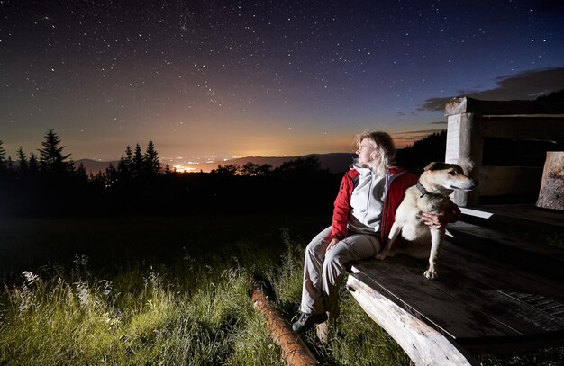 Jeune femme dans les montagnes regardant la belle nuit étoilée depuis un porche de cabane en bois