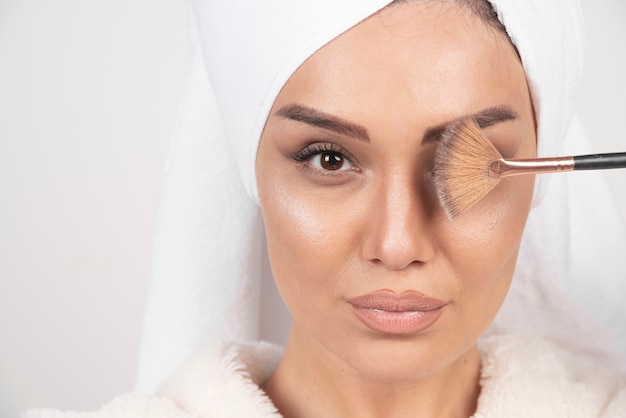 Jeune femme dans un peignoir tenant un pinceau de maquillage.