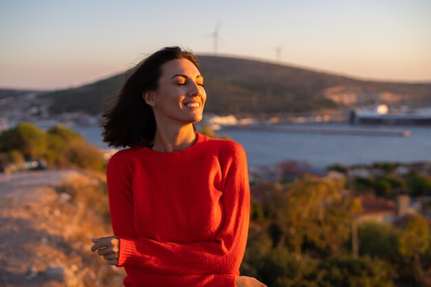 Jeune femme dans un pull rouge à un magnifique coucher de soleil sur la montagne