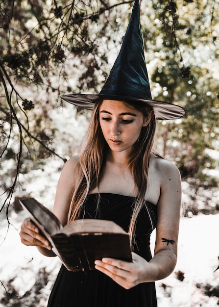 Jeune femme, dans, sorcière, chapeau, lecture, livre, dans, forêt