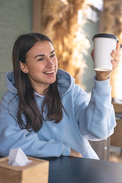 Une jeune femme dans un sweat à capuche bleu apprécie le café le matin dans un café