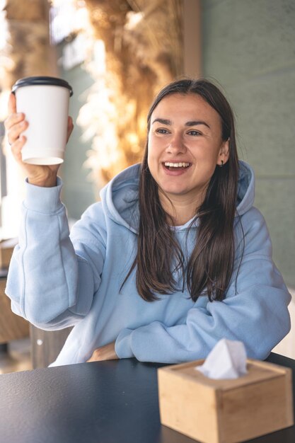 Une jeune femme dans un sweat à capuche bleu apprécie le café le matin dans un café