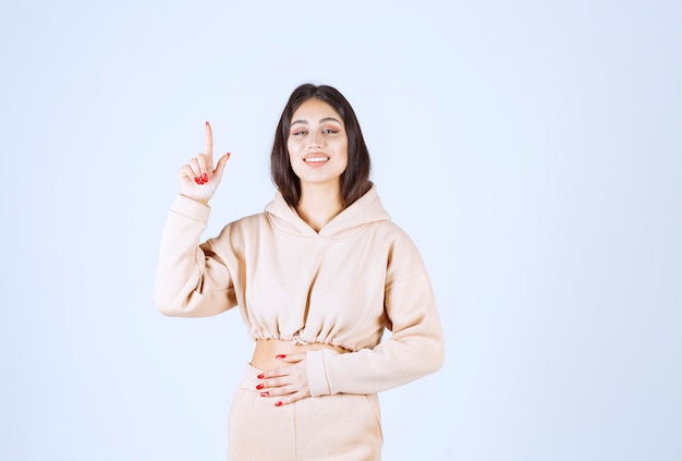 Jeune femme dans un sweat à capuche rose pointant quelque part au-dessus