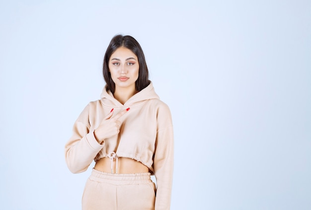 Jeune femme dans un sweat à capuche rose pointant quelque part sur la droite