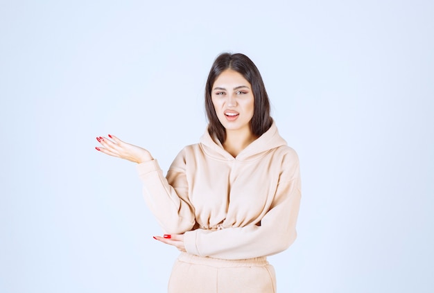 Jeune femme dans un sweat à capuche rose présentant quelque chose dans sa main ouverte