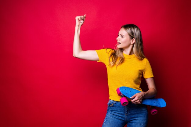 Jeune femme, dans, tenue décontractée, tenue, skateboard, projection, biceps, quoique, debout, contre, mur rouge