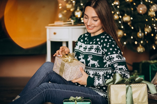 Jeune femme déballant le cadeau de Noël près du sapin de Noël