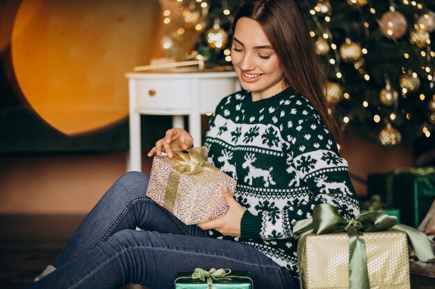 Jeune femme déballant le cadeau de Noël près du sapin de Noël