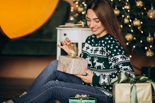 Jeune femme déballant le cadeau de Noël près du sapin de Noël