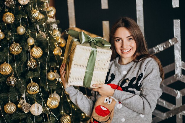 Jeune femme déballant le cadeau de Noël près du sapin de Noël