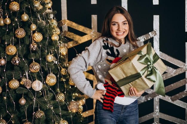 Jeune femme déballant le cadeau de Noël près du sapin de Noël