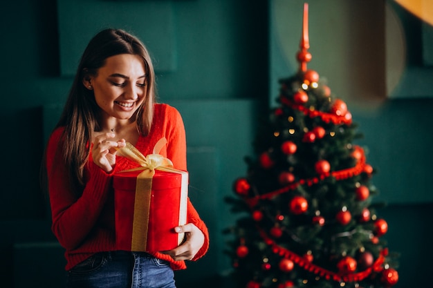 Jeune femme déballant le cadeau de Noël près du sapin de Noël