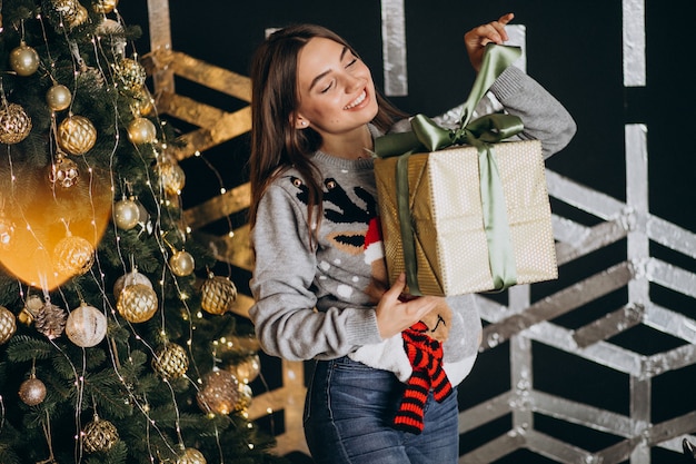 Jeune femme déballant le cadeau de Noël près du sapin de Noël