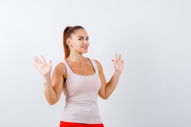 Jeune femme en débardeur beige montrant le numéro dix et à la joyeuse, vue de face.