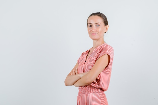 Jeune femme debout avec les bras croisés en robe rayée et à la recherche positive. vue de face.