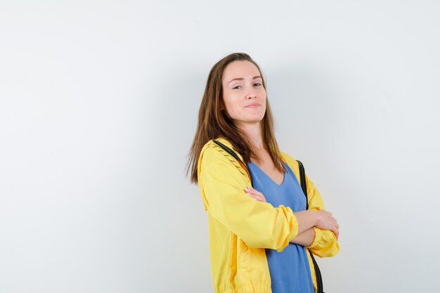 Jeune femme debout avec les bras croisés en t-shirt et l'air confiant, vue de face.