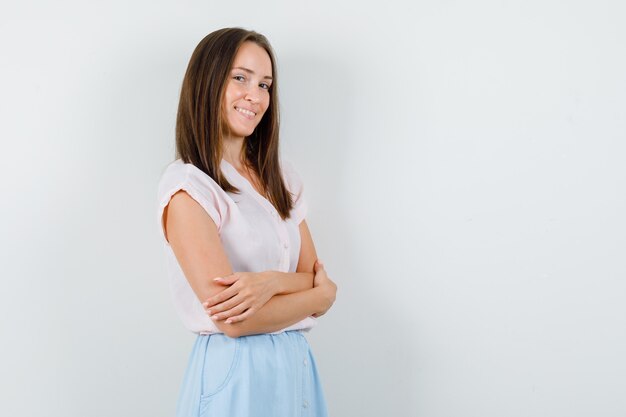 Jeune femme debout avec les bras croisés en t-shirt, jupe et à la joyeuse. vue de face.