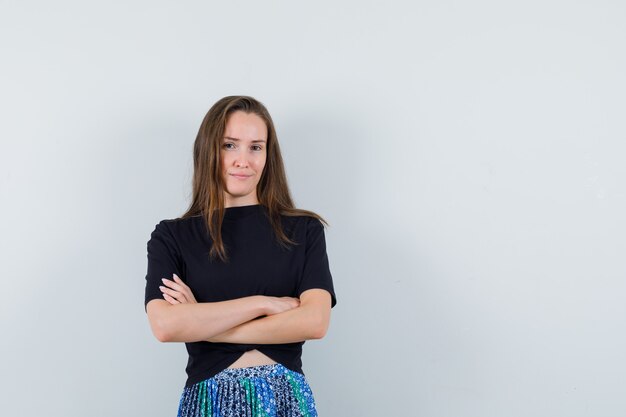 Jeune femme debout avec les bras croisés en t-shirt noir et jupe bleue et à la confiance