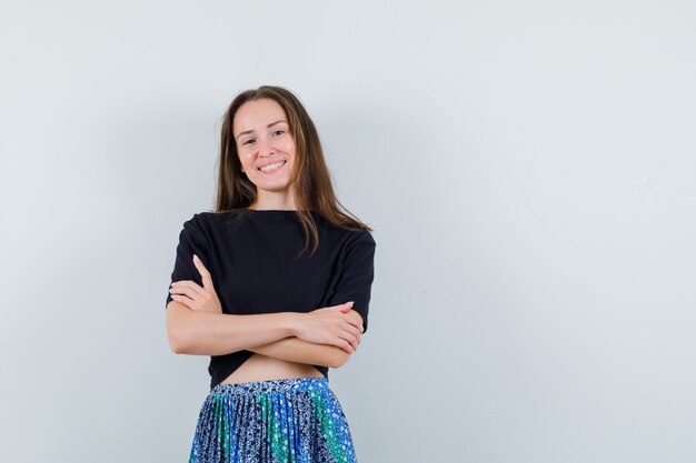 Jeune femme debout avec les bras croisés en t-shirt noir et jupe bleue et à la recherche attrayante