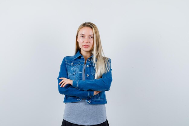 Jeune femme debout avec les bras croisés en t-shirt, veste en jean, jupe et l'air confiant.