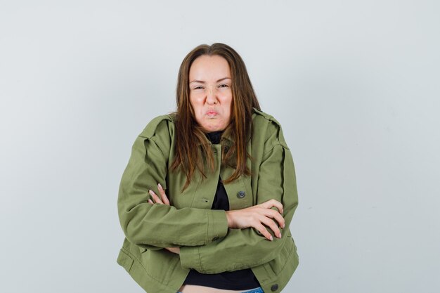 Jeune femme debout avec les bras croisés tout en aigri son visage en veste verte et à la mécontentement. vue de face.