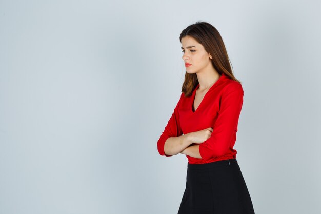 Jeune femme debout avec les bras croisés tout en regardant ailleurs en chemisier rouge