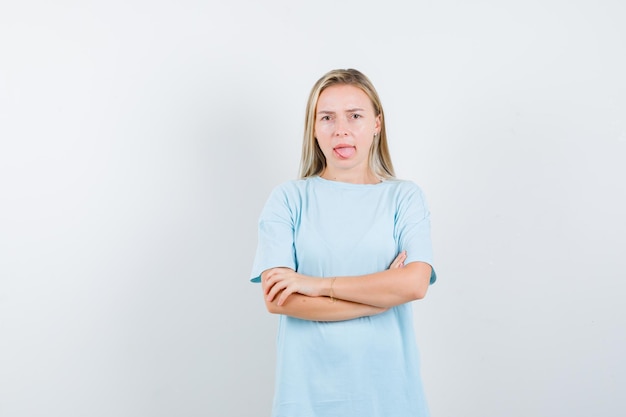 Jeune femme debout avec les bras croisés tout en tirant la langue isolée