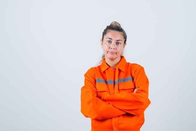 Jeune femme debout avec les bras croisés en uniforme de travailleur et à la recherche d'hésitant. vue de face.