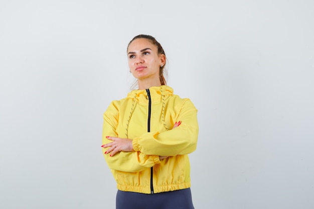 Jeune femme debout avec les bras croisés en veste jaune et à la pensive. vue de face.