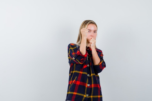 Jeune femme debout dans la lutte contre la pose en chemise à carreaux et à la vue de face confiante.