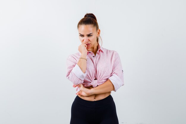 Jeune femme debout dans la pensée pose en chemise décontractée et regardant pensif, vue de face.