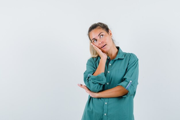 Jeune femme debout dans la pensée pose en chemisier vert et à la pensif