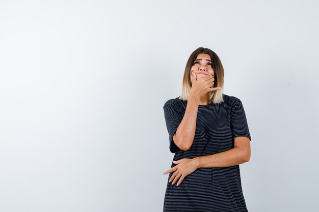 Jeune femme debout dans la pensée pose en robe polo et à la vue de face, hésitante.