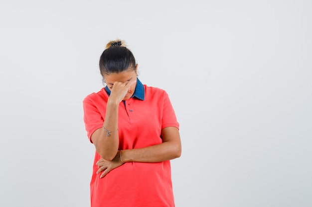 Jeune femme debout dans la pensée pose en t-shirt rouge et regardant pensif, vue de face.