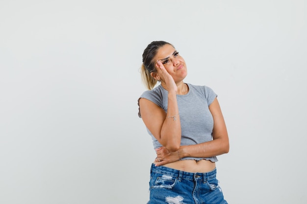 Jeune femme debout dans la pensée pose en t-shirt, short et à la recherche hésitante.