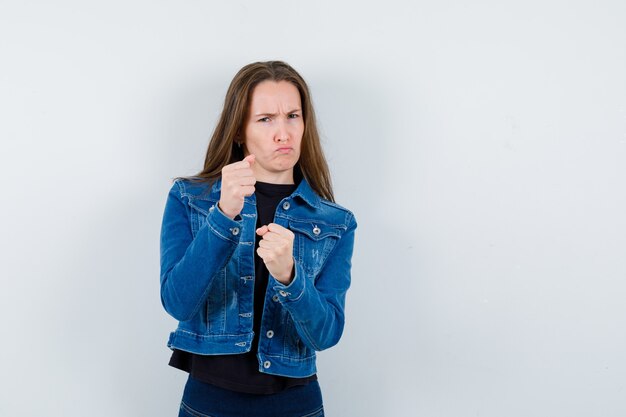 Jeune femme debout dans la pose de combat en chemisier, veste et l'air confiant, vue de face.