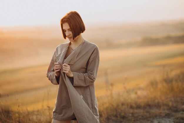 Jeune femme debout dans la prairie au coucher du soleil