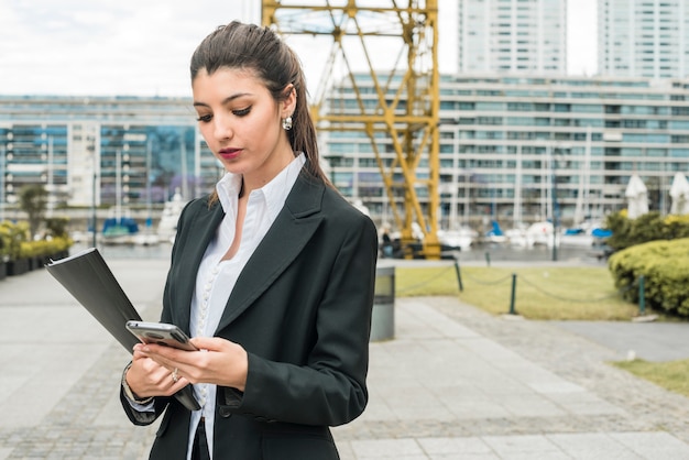 Photo gratuite jeune femme debout devant le bâtiment à l'aide de téléphone portable