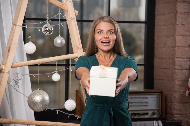 Une jeune femme debout et donnant un cadeau de Noël près des boules de Noël