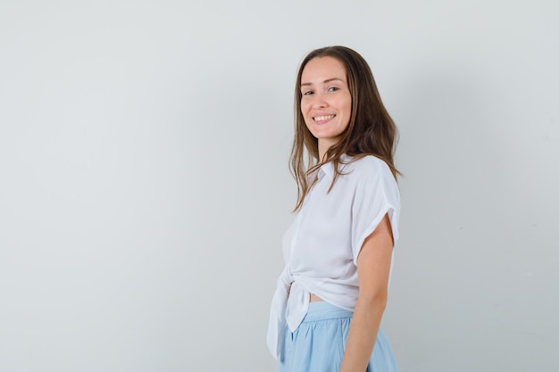 Jeune femme debout droite et posant à l'avant en chemisier blanc et jupe bleu clair et à la joyeuse