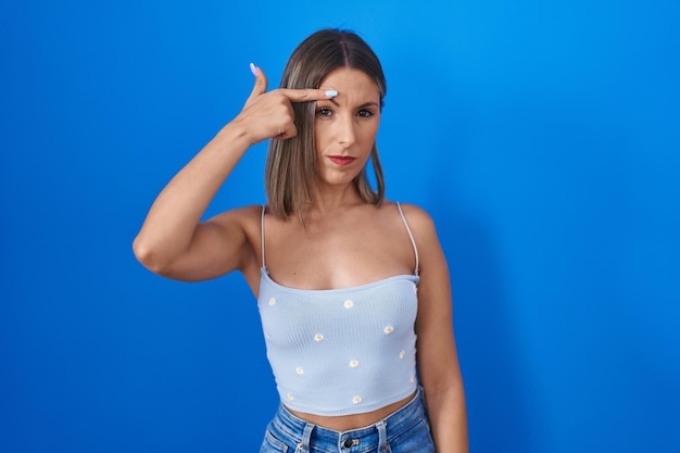 Photo gratuite jeune femme debout sur fond bleu pointant mécontent de bouton sur le front, infection laide de point noir. acné et problème de peau