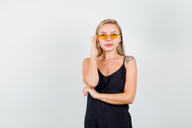 Jeune femme debout avec la main sur des lunettes en maillot noir et à la confiance.