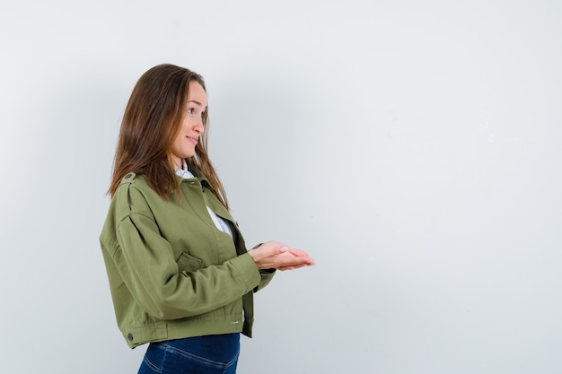 Jeune femme debout avec les mains en coupe en chemisier, veste et semblant délicate.