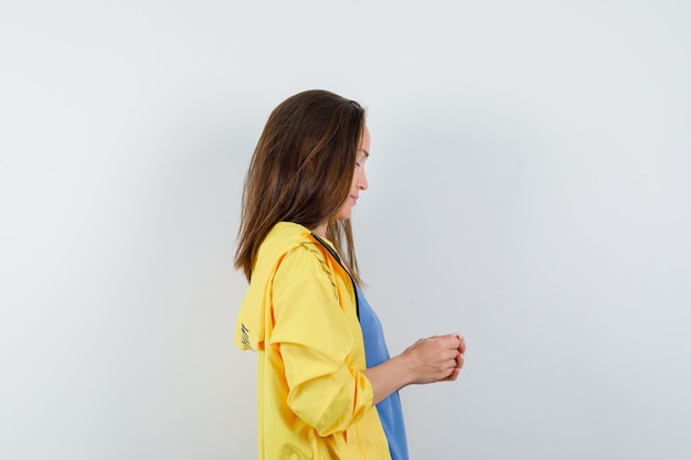 Jeune Femme Debout Avec Les Mains Jointes En T-shirt, Veste Et à La Pensive.