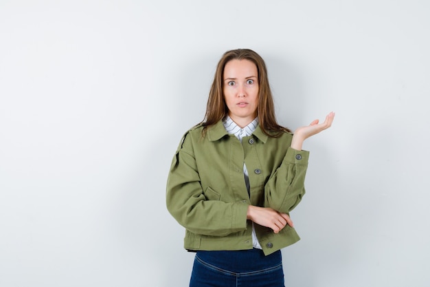 Jeune femme debout avec la paume écartée en chemisier, veste et à la perplexité.