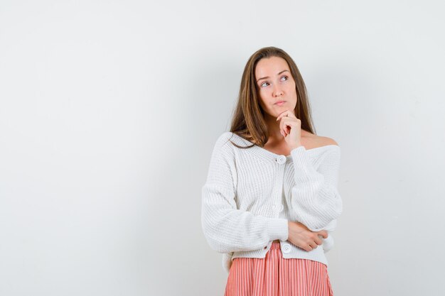 Jeune femme debout en pensant poser en cardigan et jupe à la recherche d'isolement hésitant