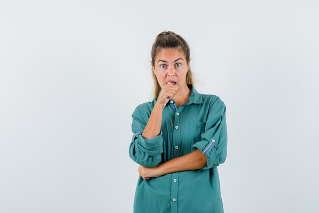 Jeune femme debout en pensant poser et mettre la main sur la bouche en chemisier vert et à la pensif