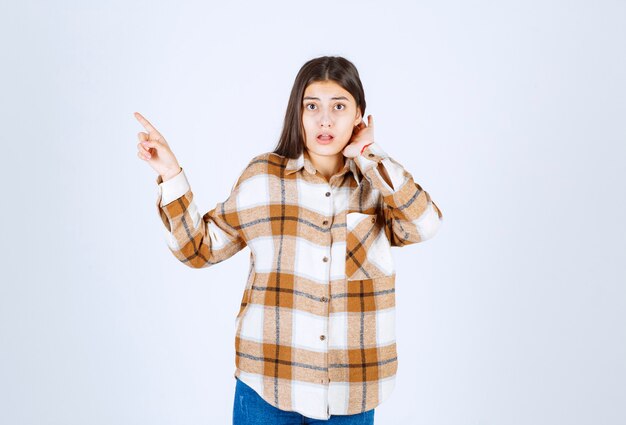 jeune femme debout et pointant quelque part sur un mur blanc.