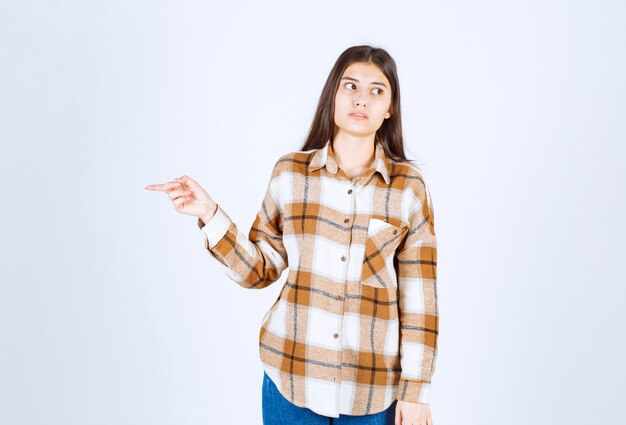 jeune femme debout et pointant quelque part sur un mur blanc.