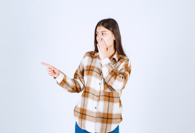 jeune femme debout et pointant quelque part sur un mur blanc.